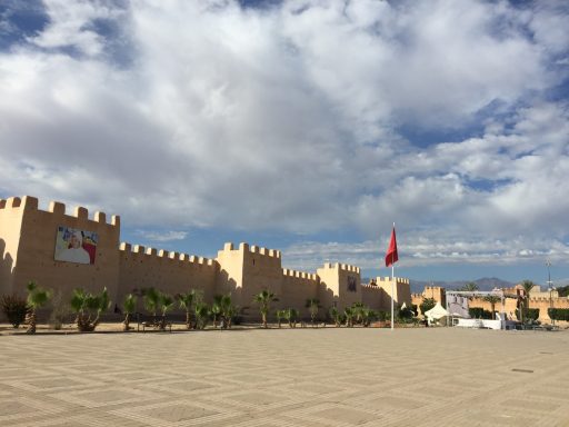 A fortified building with a red flag and cloudy blue sky in the background.