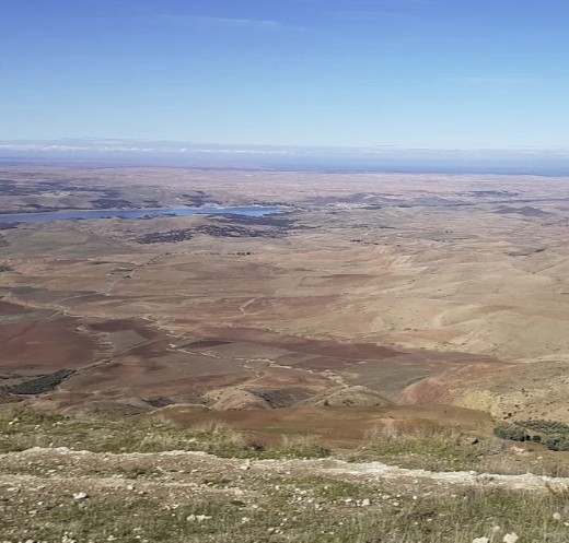 Panoramic view of a vast, arid landscape with distant hills and a blue lake.