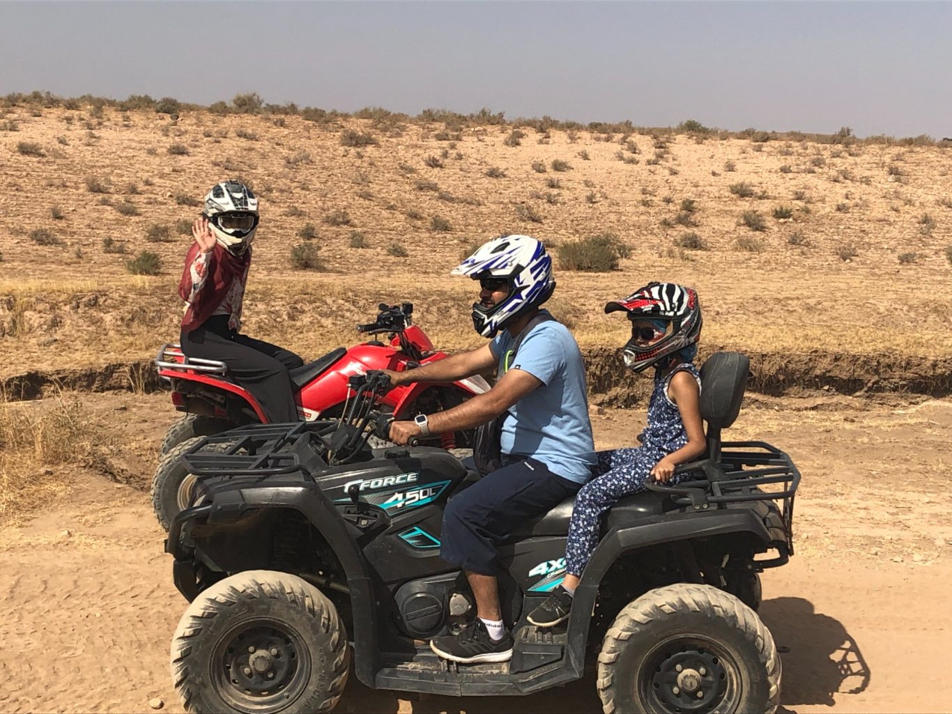 Two adults and a child riding quad bikes in a desert landscape.