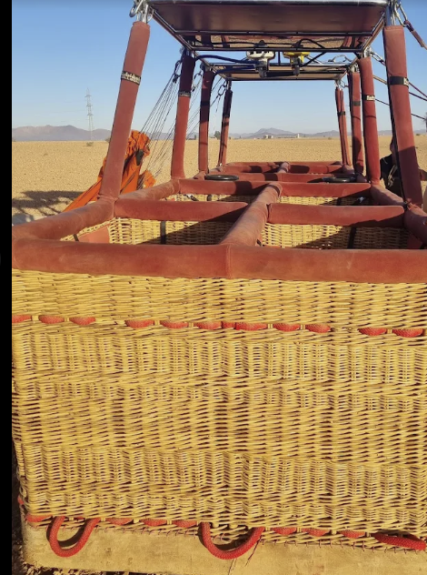 Basket of a hot air balloon, made of wicker, set against a clear sky.