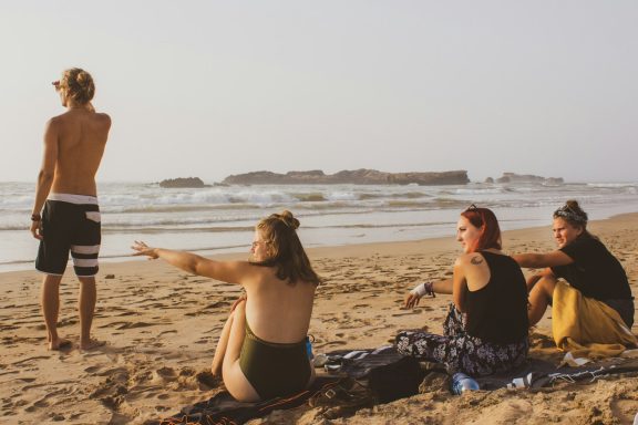 A group of four friends relaxing on the beach, looking out at the ocean.