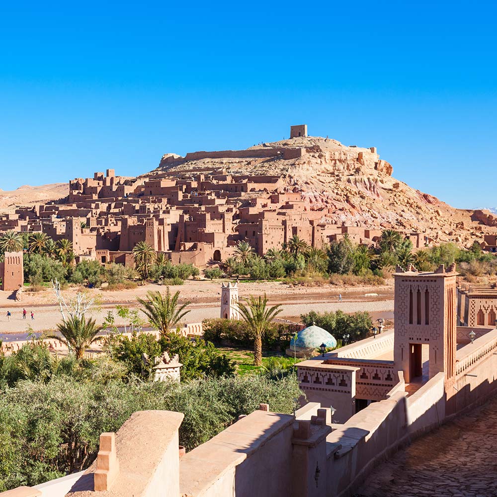 Ait Ben Haddou Historic mudbrick village on a hillside with surrounding palm trees and clear blue sky.