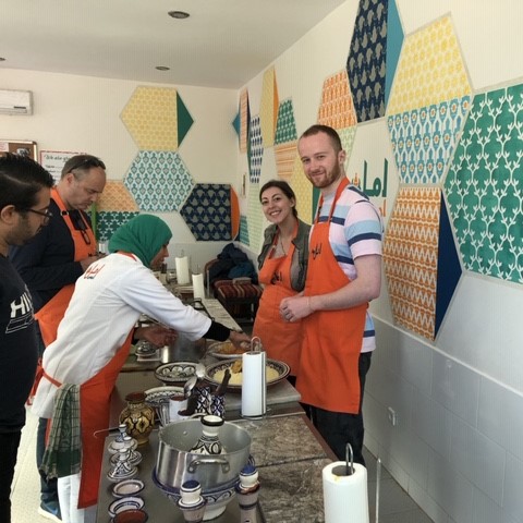 A group of people in aprons preparing food in a colourful cooking class environment.