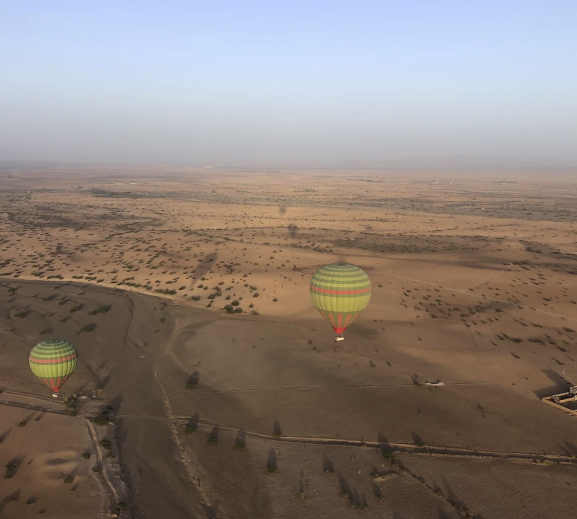 Hot air balloons floating over a vast, arid landscape at sunrise.