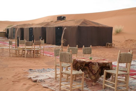 A desert campsite with tents, tables, and chairs set up on sandy terrain.