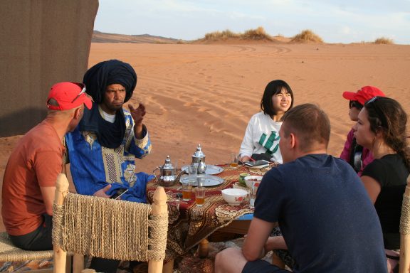 Group enjoying tea and conversation in a desert setting with traditional attire.