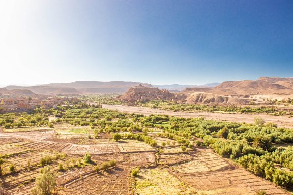 Expansive landscape with mountains, green fields, and a clear blue sky.