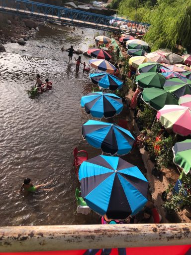 River scene with people swimming and colourful umbrellas along the bank.